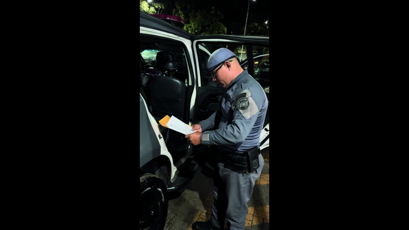 Policial consultando documentos junto à viatura